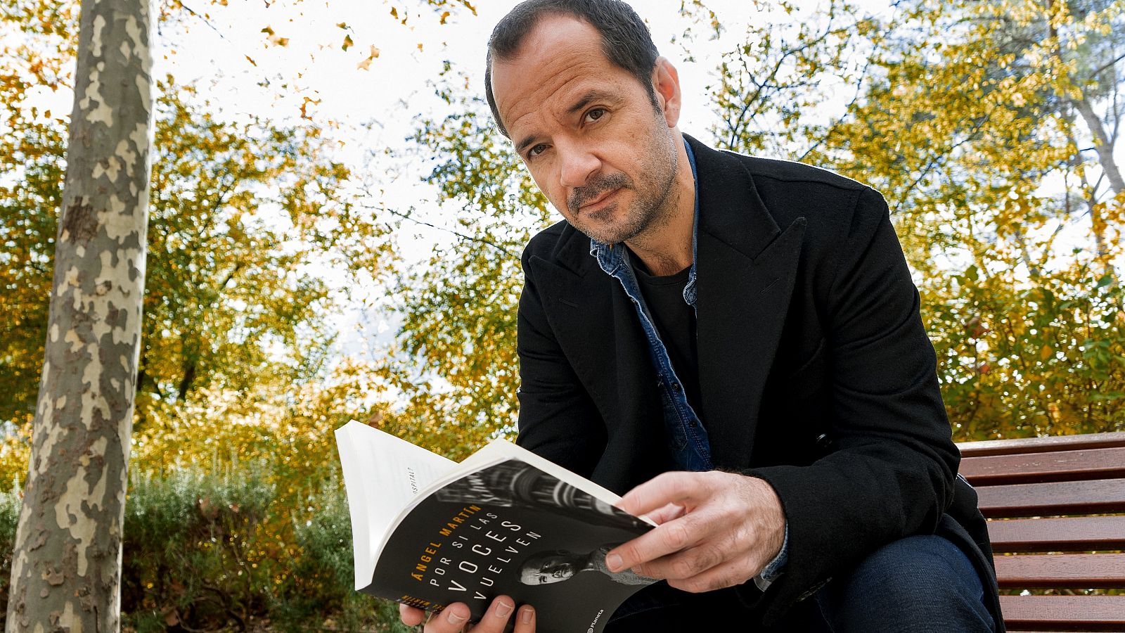 Ángel Martín lee en un banco de un parque su libro "Por si las voces vuelven"