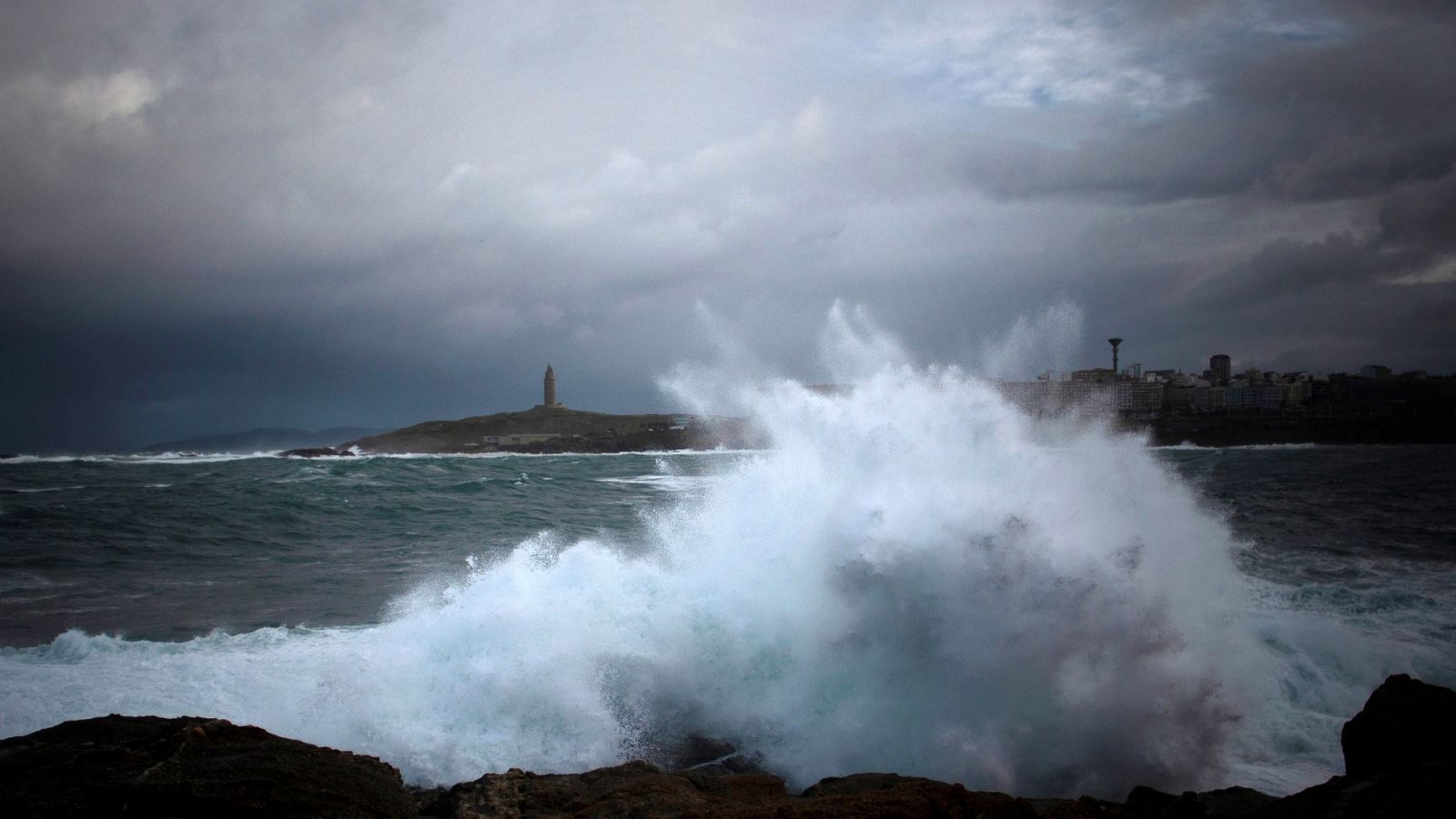 Las olas del mar golpean la costa de A Coruña, con la Torre de Hérculas al fondo a la izquierda