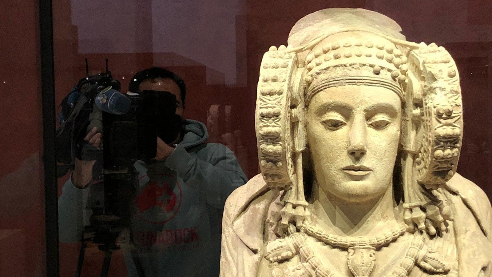 Un cámara de TVE graba la Dama de Elche y se refleja en el cristal que protege la pieza arqueológica.