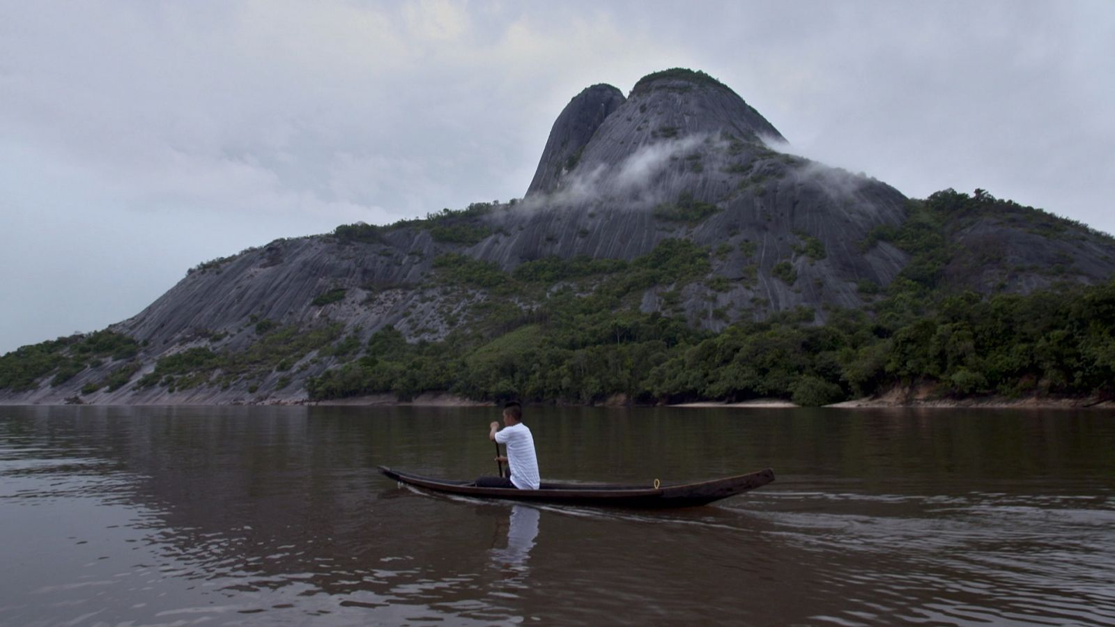  Un home amb una canoa i darrere una petita muntanya envoltada de boira