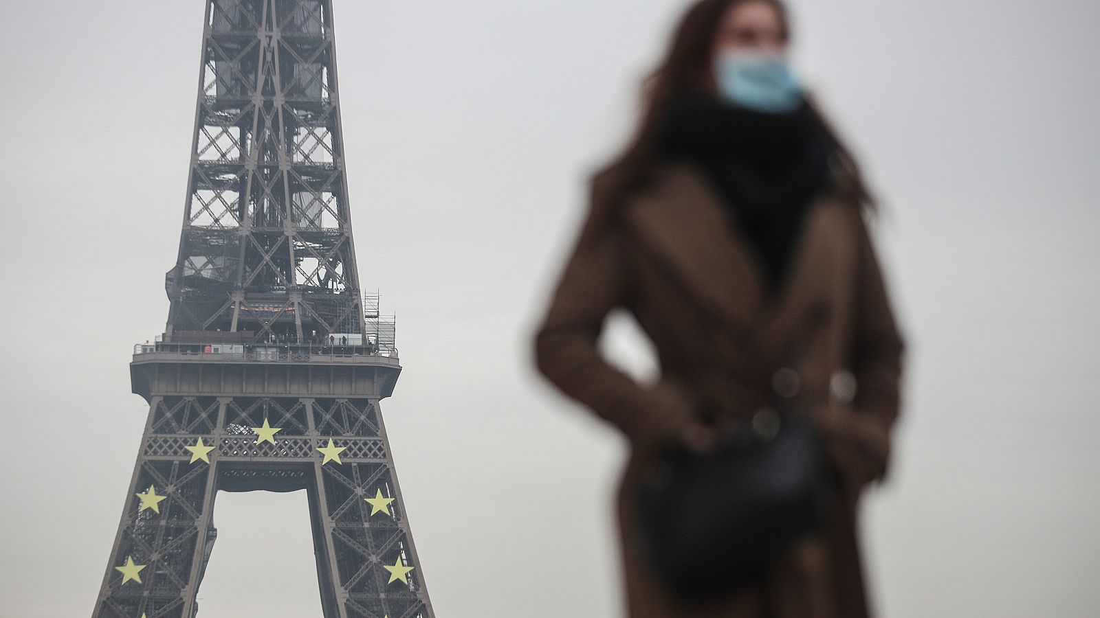 Una mujer con mascarilla pasea junto a la Torre Eiffel de Paris.