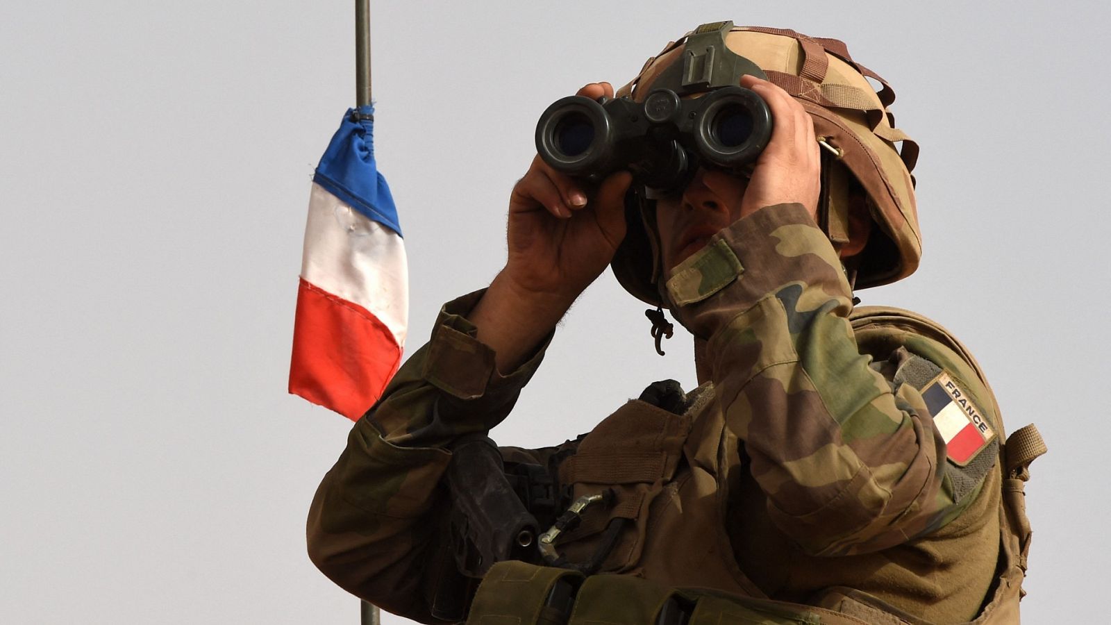 Un soldado mira a través de unos prismáticos con la bandera francesa de fondo