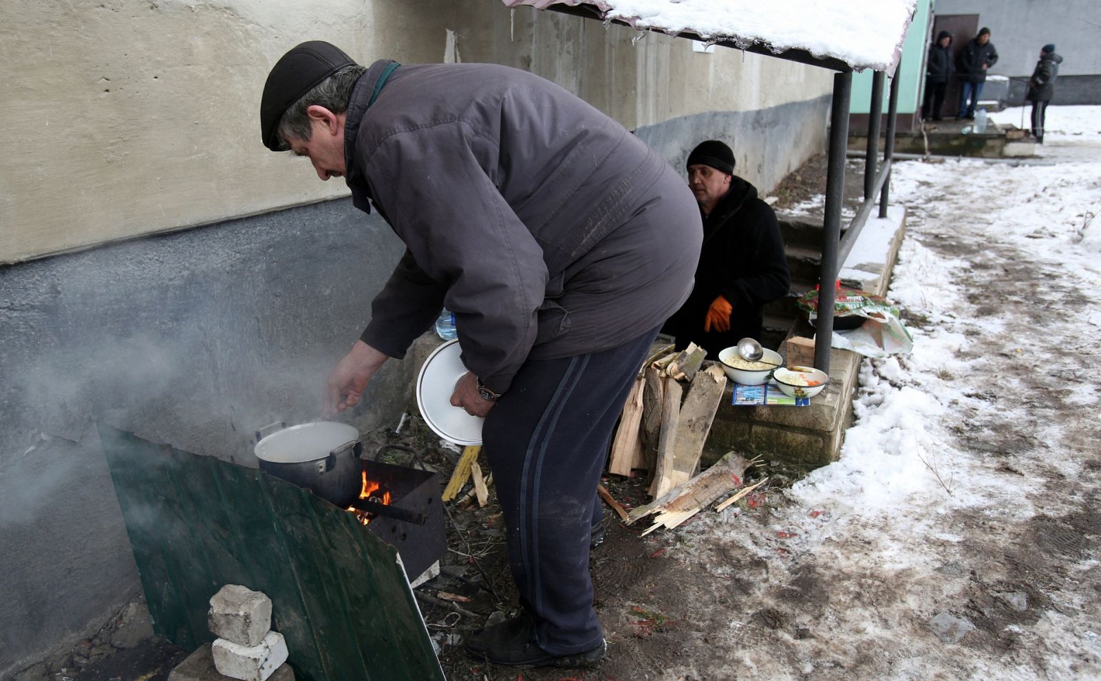 Un residente local prepara su comida en un fuego fuera de un edificio de apartamentos en la ciudad de Popasna, región de Lugansk