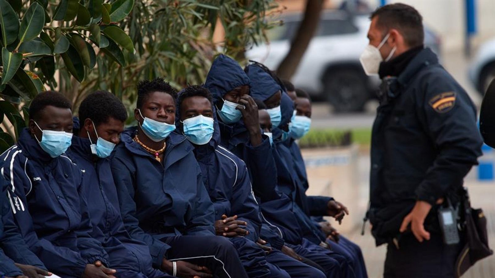 Un grupo de migrantes esperan junto a la Jefatura de la Policia Nacional de Melilla.