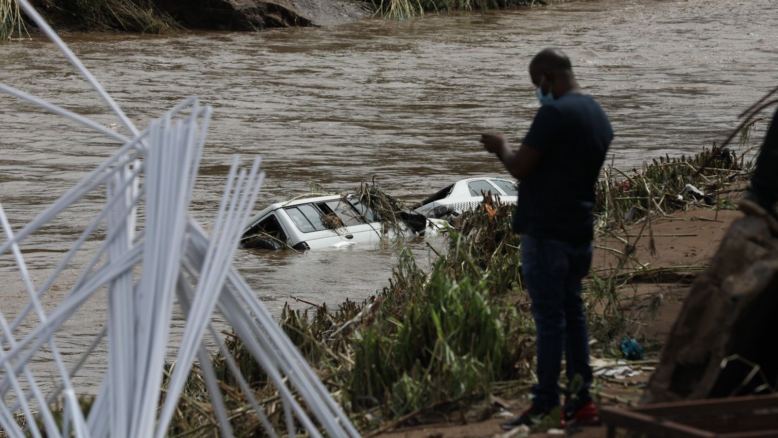 Un hombre observa dos vehículos sumergidos en el agua cerca de Durban, en Sudáfrica.