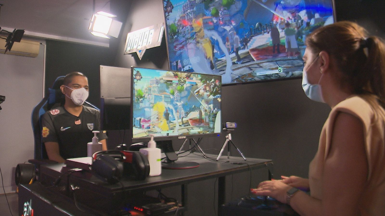 Una reportera entrevista a un jugador de videojuegos rodeados de pantallas