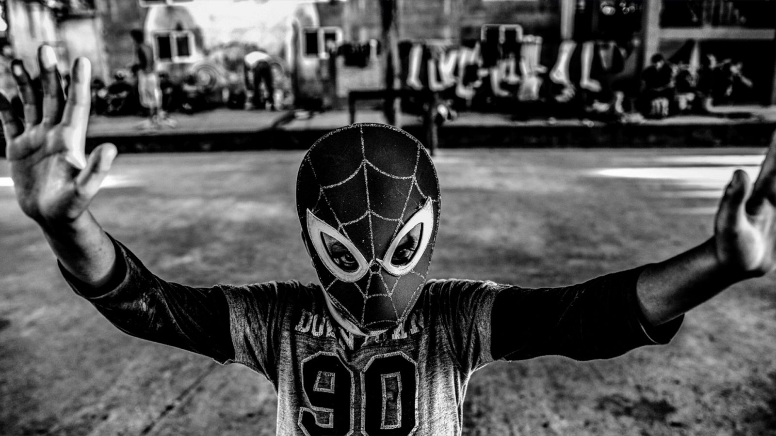 Un niño con la careta de Spiderman levanta las manos en la calle