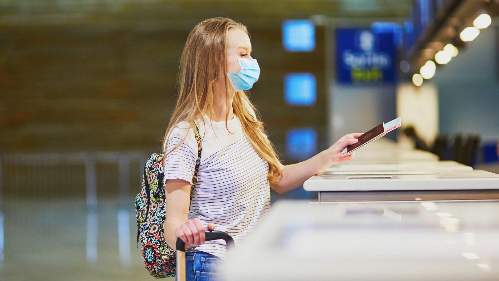 Una joven con mascarilla por la pandemia de COVID-19 sostiene su pasaporte en un aeropuerto.