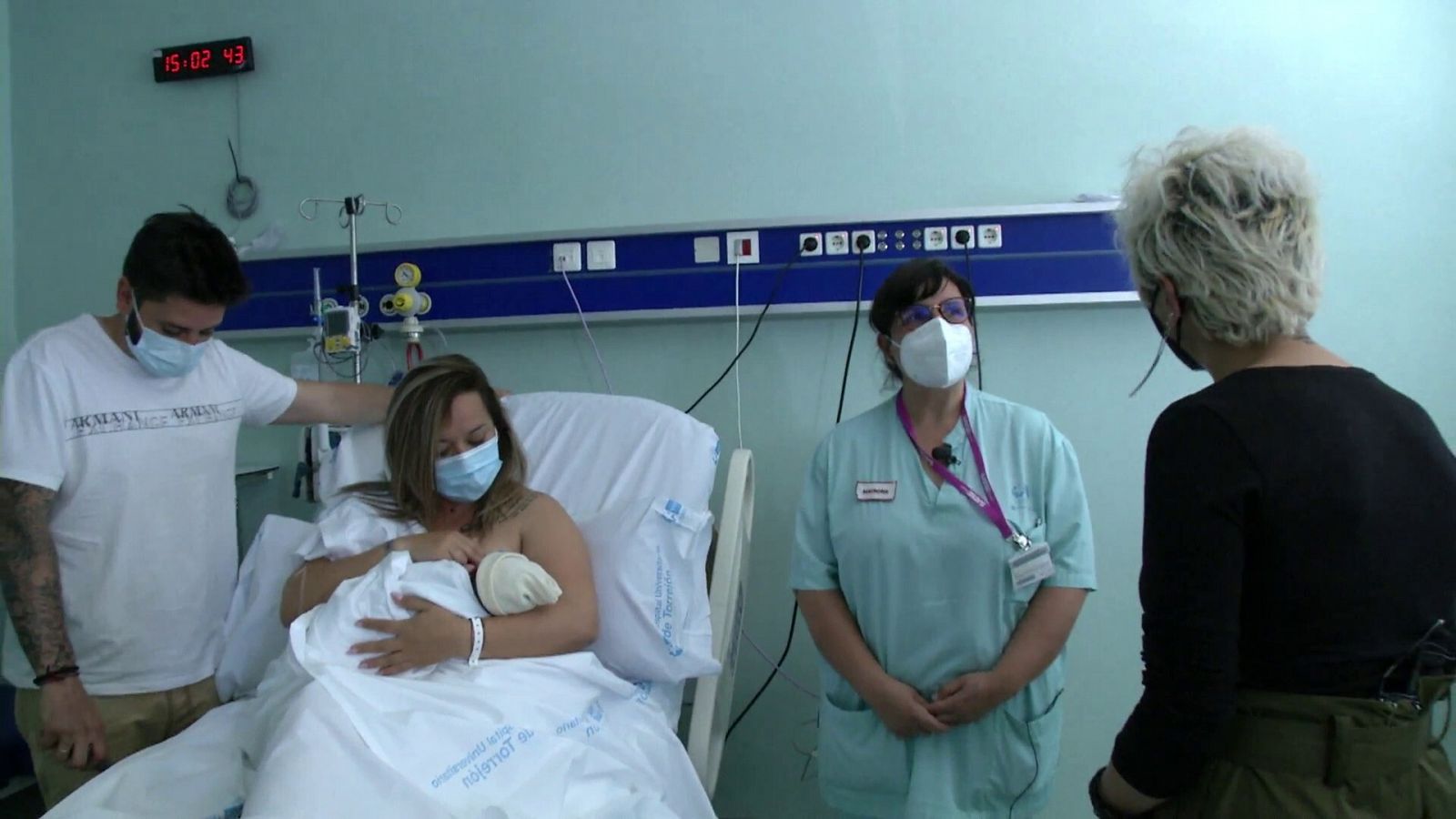 Una madre amamanta a su bebé en la cama del hospital acompañada de su pareja, una sanitaria y la reportera de RTVE.