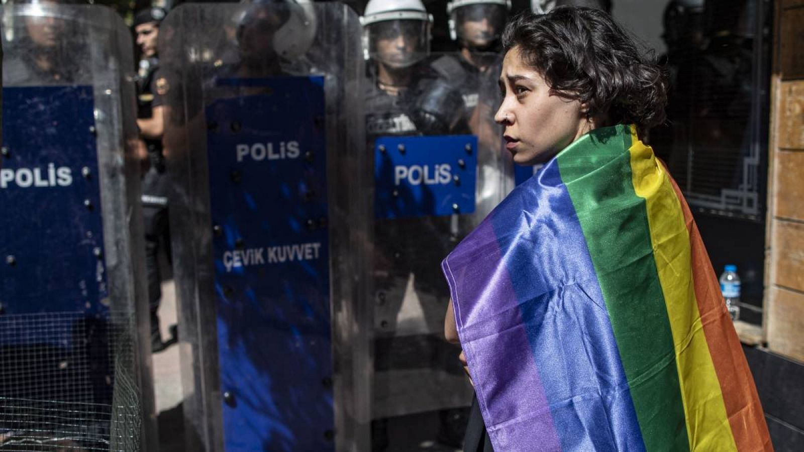 Un partidario de la comunidad LGBT sostiene una bandera con los colores del arco iris mientras la policía turca bloquea una calle durante la Marcha del Orgullo de Estambul, Turquía. 