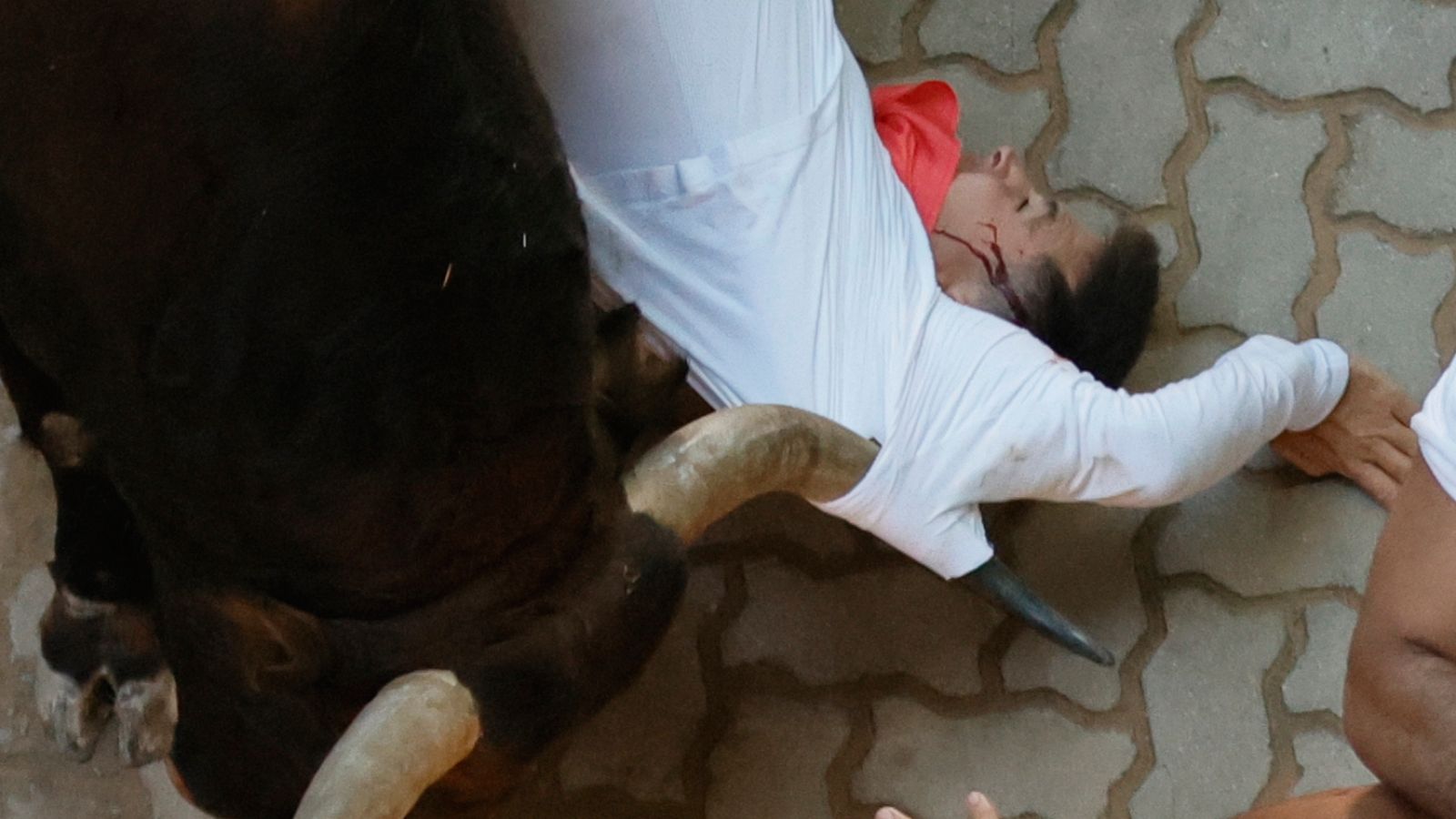 Un toro de la ganadería pacense de Jandilla arrastra a un mozo a su paso por el callejón durante el sexto encierro de los Sanfermines