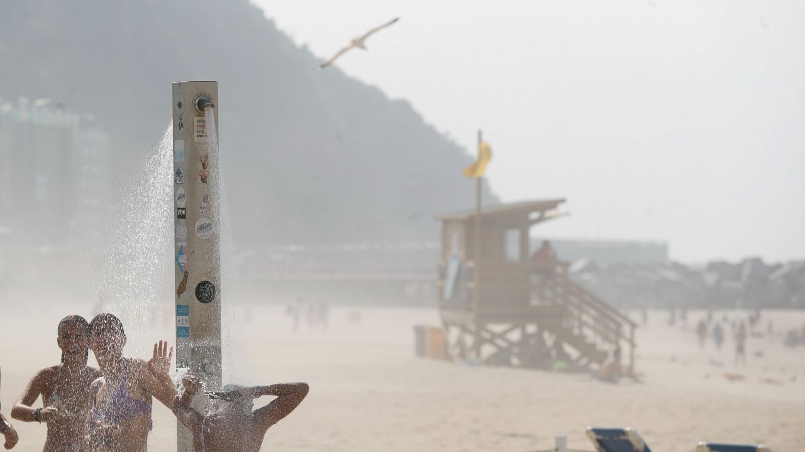 Varios jóvenes se duchan este lunes en la playa de La Zurriola de San Sebastián, donde tras un día de intenso calor una galerna ha bajado la temperatura en pocos minutos. EFE/ Juan Herrero