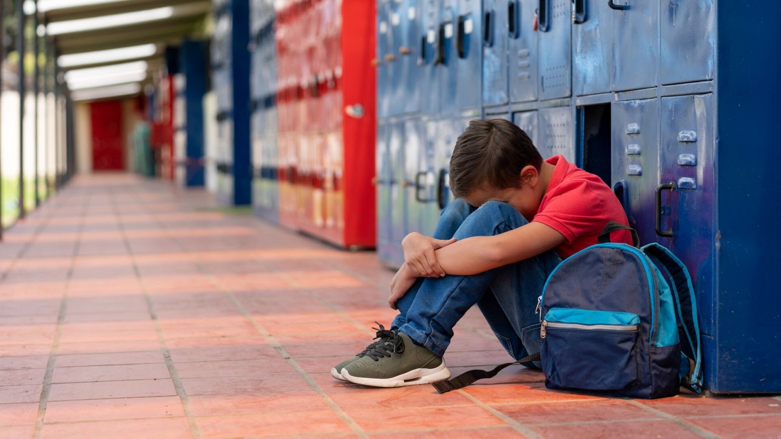 Un niño se sienta asustado en el pasillo de un instituto en una imagen de archivo