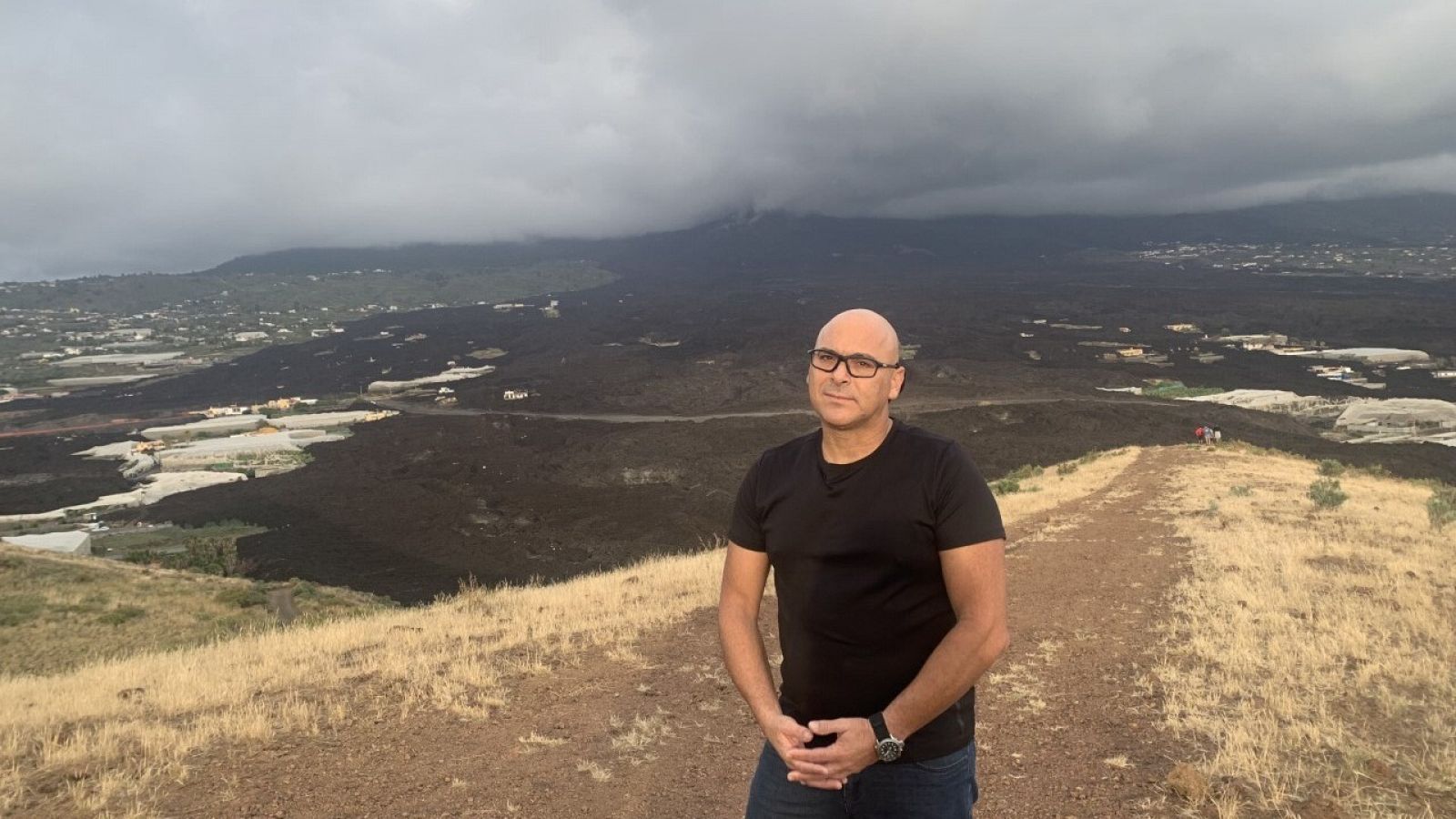 Foto de persona con camiseta negra con la colada del volcan de la Palma a su espalda.