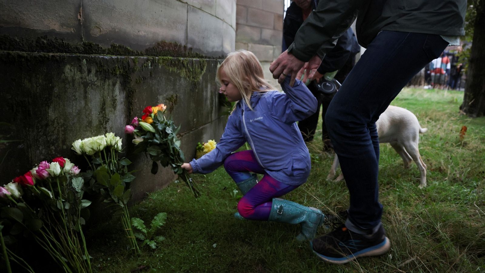 Una niña deja un ramo de flores frente al Palacio de Buckingham