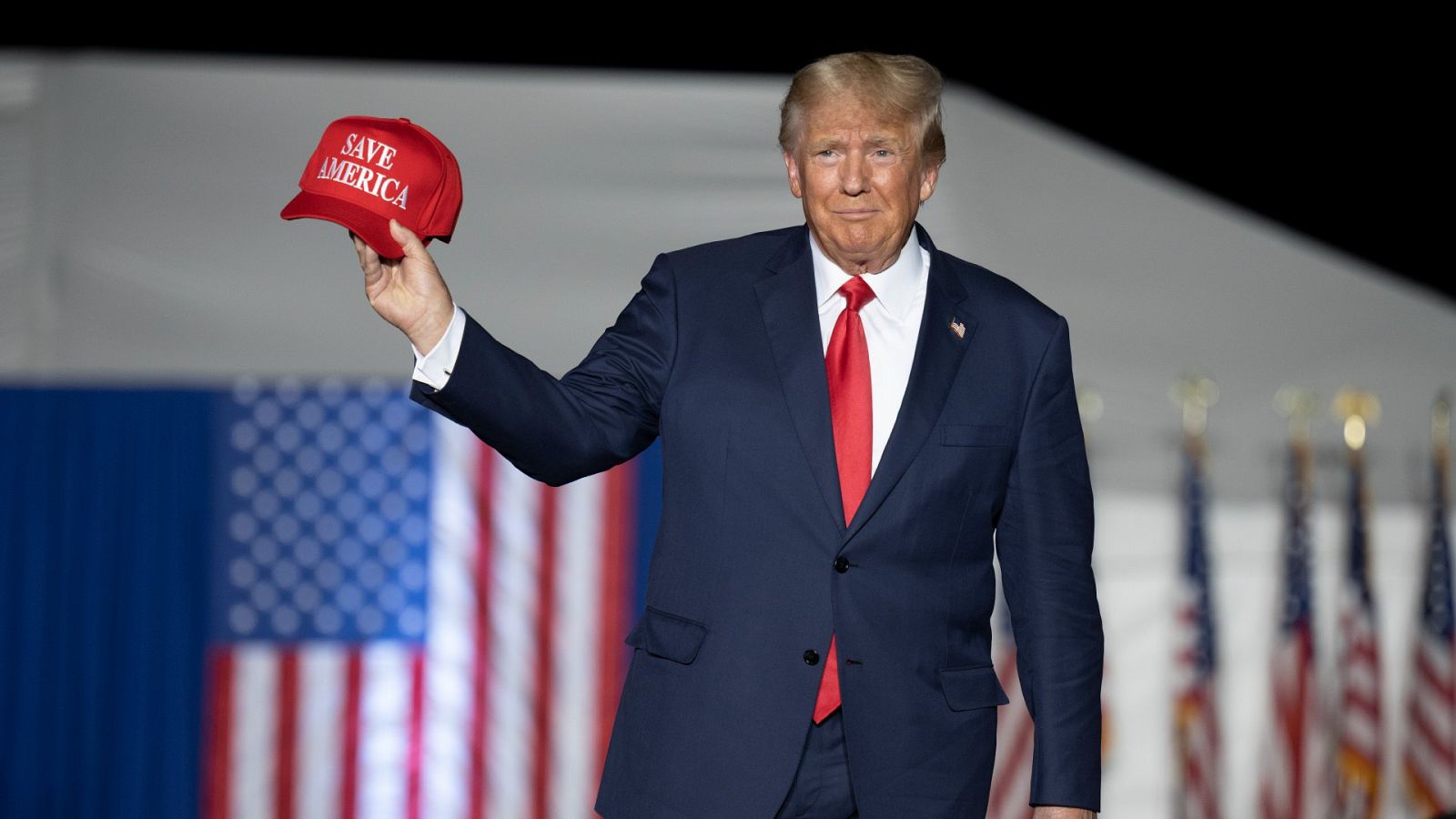 El expresidente de EE. UU., Donald Trump, con una gorra roja en la mano que dice SAVE AMERICA