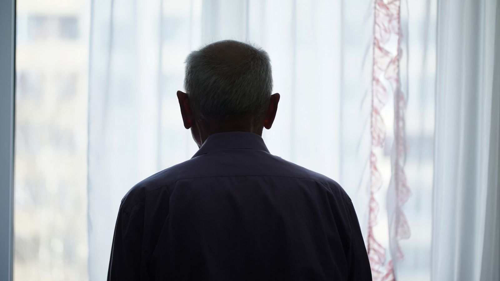 Un hombre mayor se asoma a una ventana en una imagen de archivo