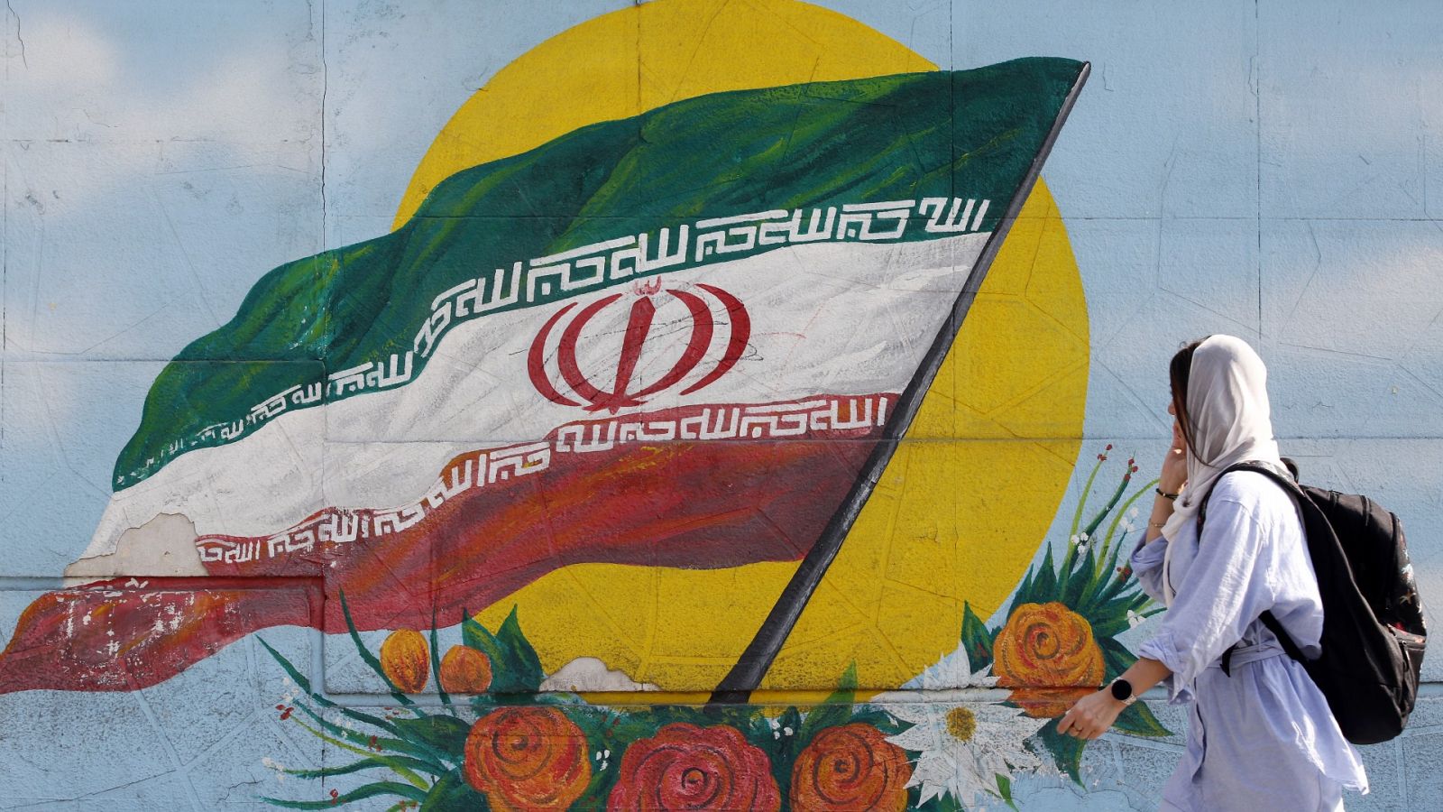 Una mujer con velo en Teherán junto a un graffiti de la bandera nacional