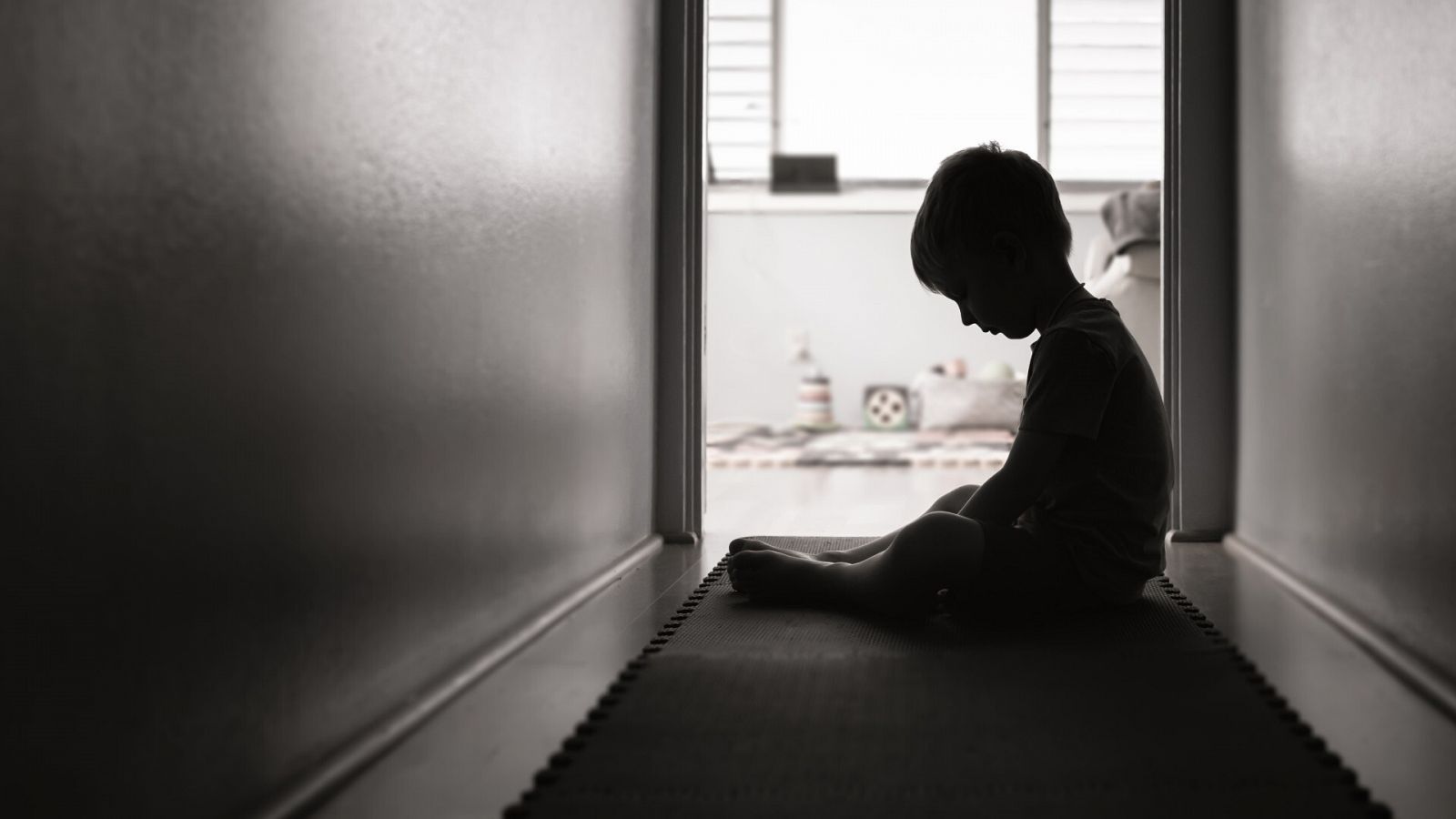 Silueta a contraluz de un niño sentado en el suelo del pasillo de una casa