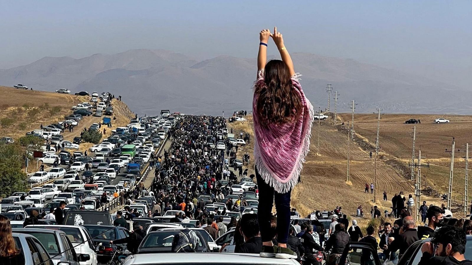 Una mujer sin velo de pie sobre un vehículo mientras miles se dirigen hacia el cementerio de la ciudad natal de Mahsa Amini