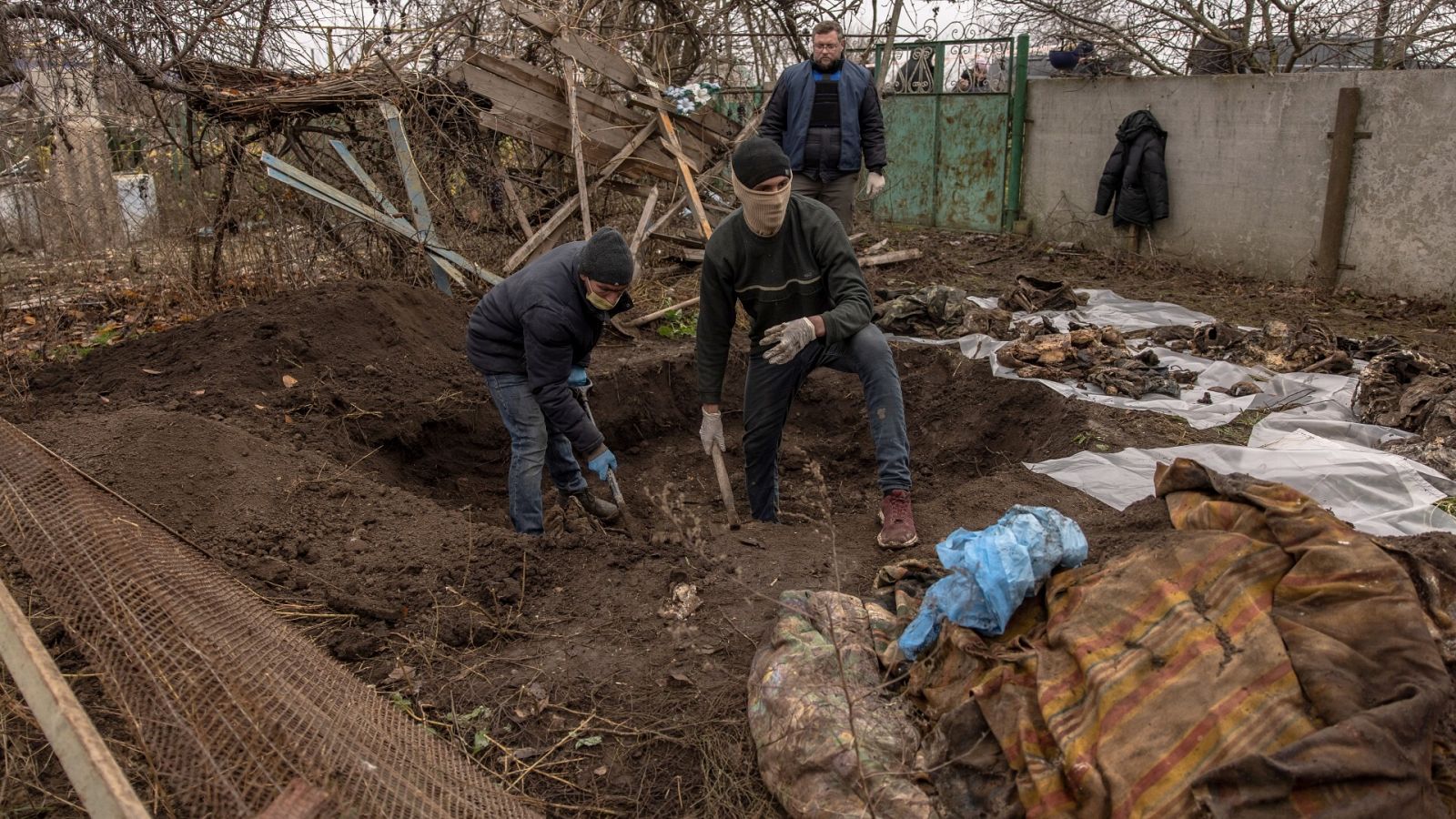 Residentes de Pravdyne, a las afueras de Jersón, ayudan a forenses e investigadores a exhumar los restos de seis personas de una fosa común, supuestamente asesinados durante la ocupación rusa de la ciudad. EFE/EPA/ROMAN PILIPEY
