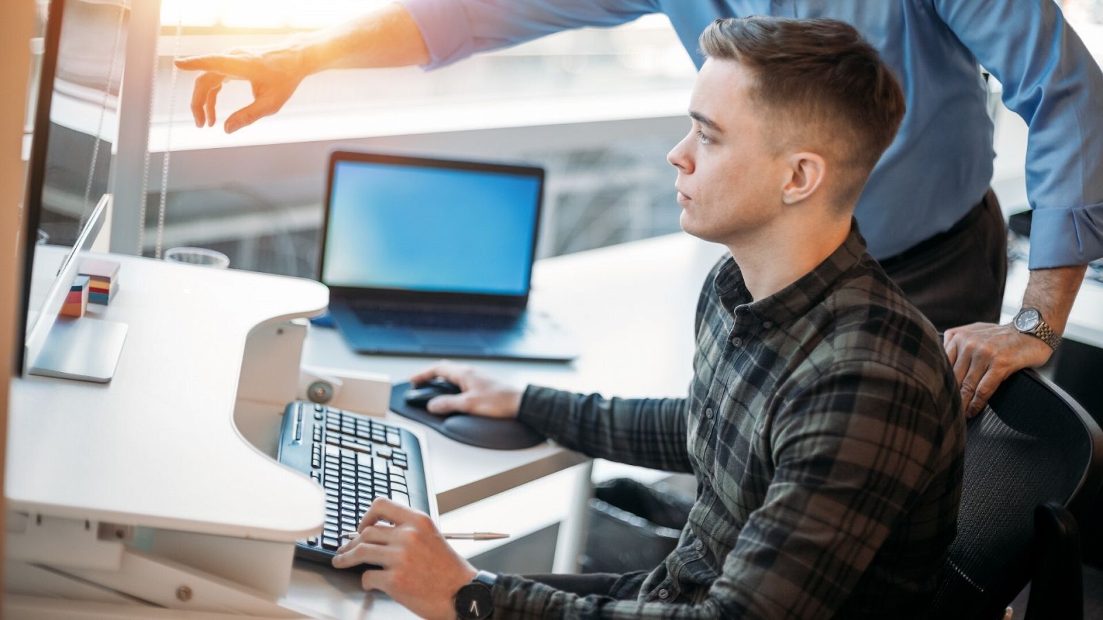 Un joven utiliza un ordenador en una oficina guiado por su tutor