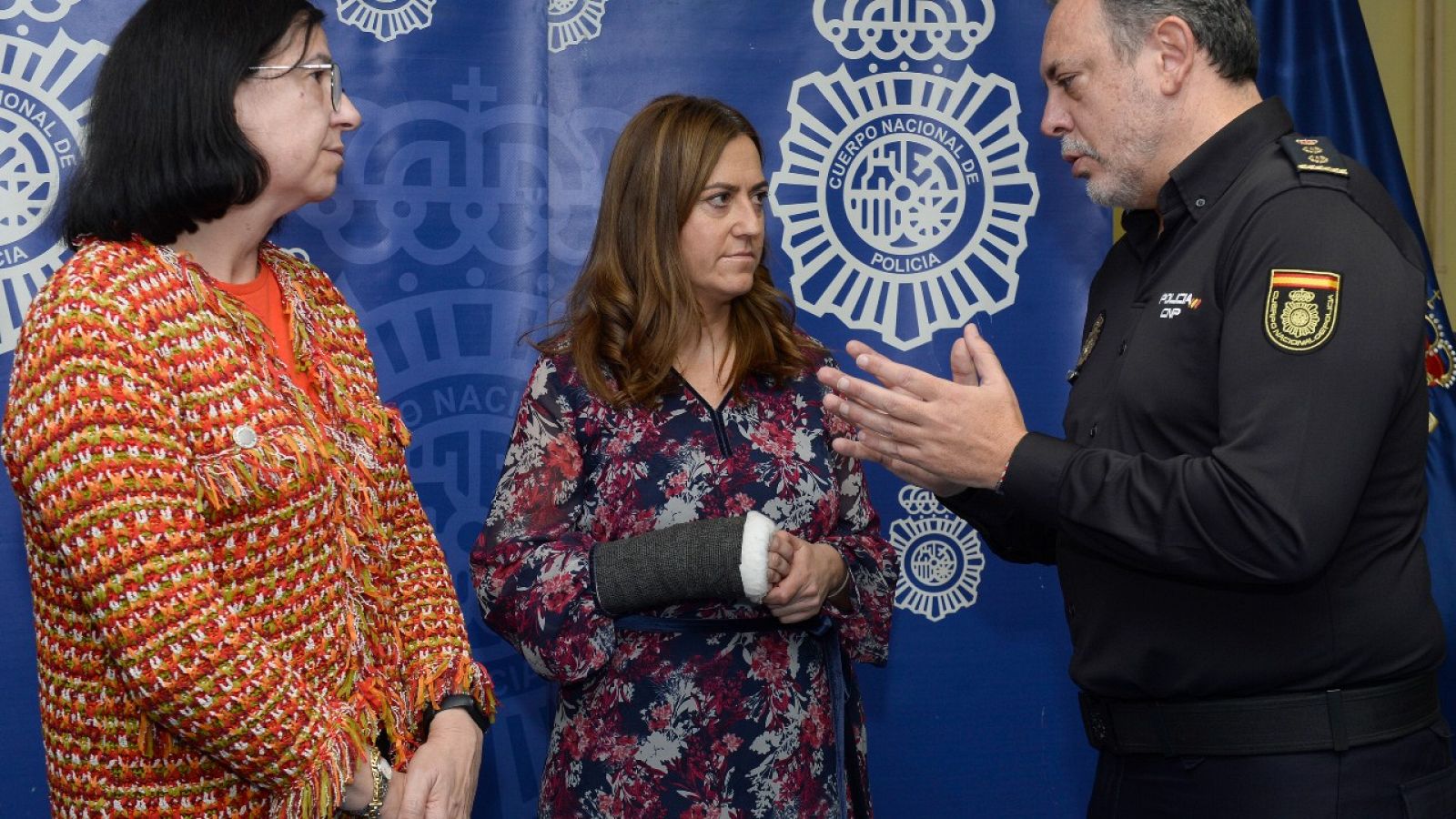 Dos mujeres y un policía nacional conversan antes de una rueda de prensa