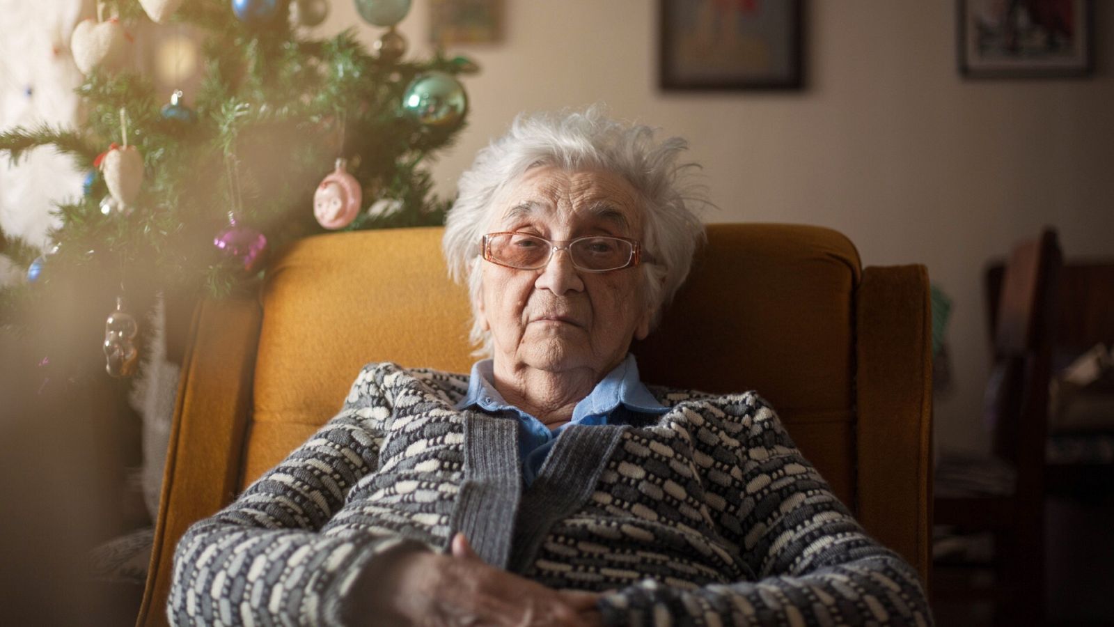 Una mujer mayor posa delante de un árbol de Navidad
