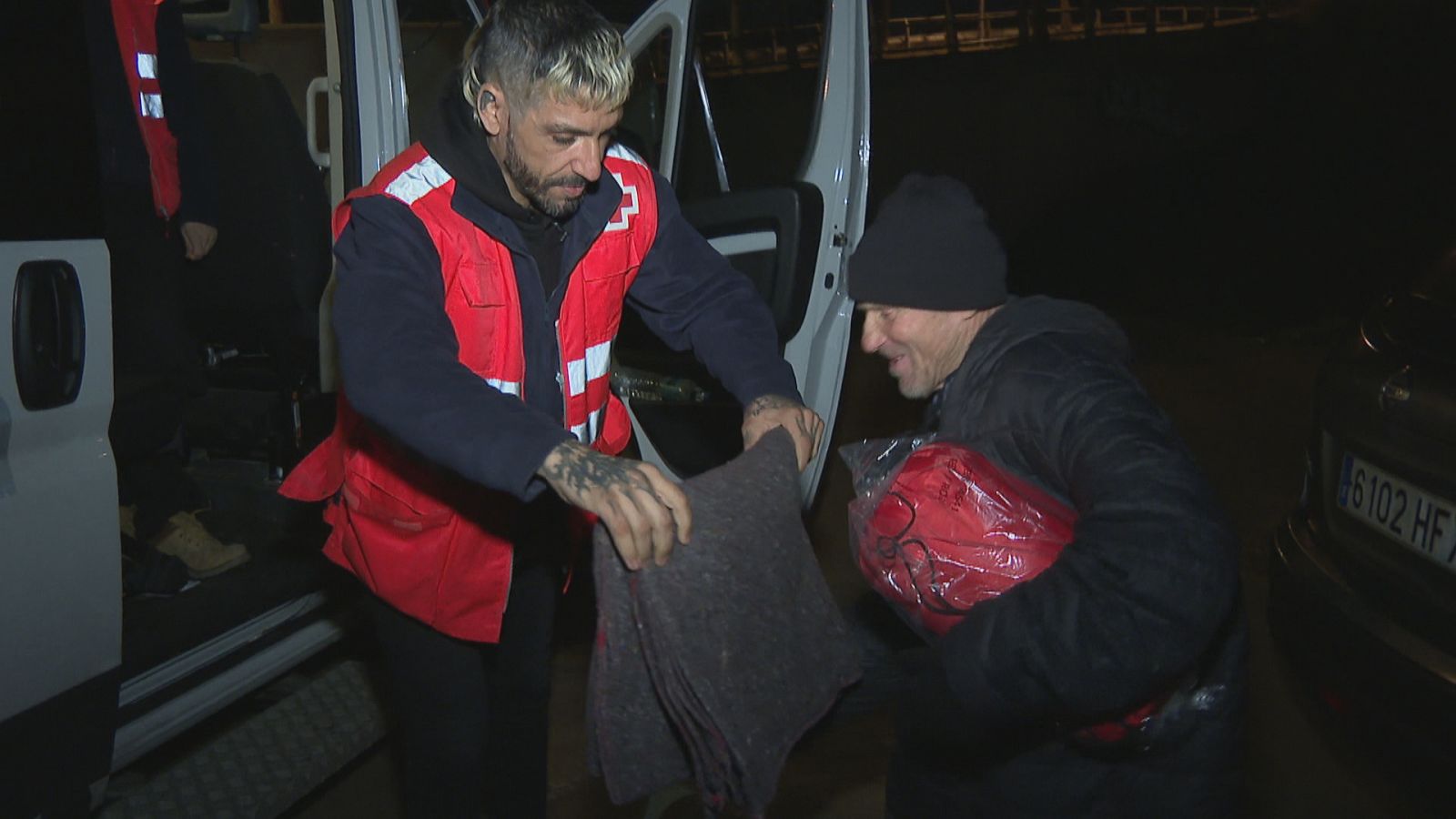 Un treballador de Creu Roja ofereix una manta a un home sense sostre
