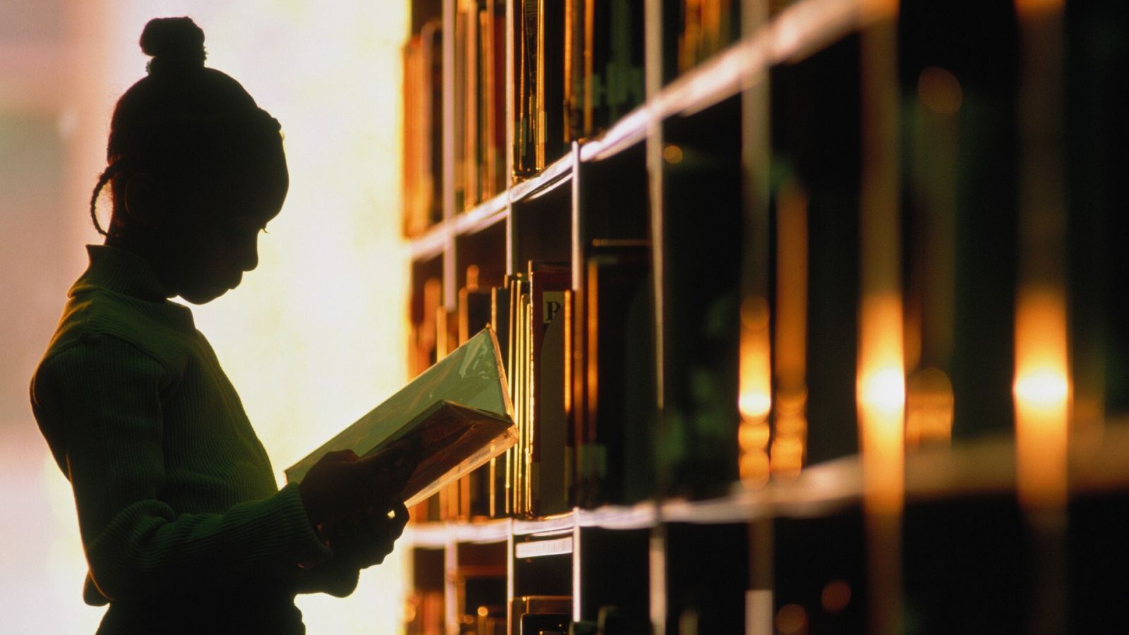 Una niña lee un libro en una biblioteca, en una imagen de archivo