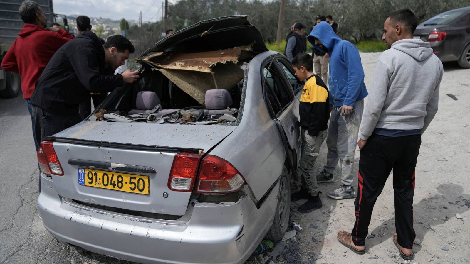 Palestinos inspeccionan el vehículo dañado en el que tres militantes palestinos fueron asesinados a tiros por las fuerzas israelíes