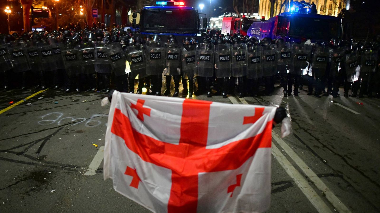 Un manifestante sostiene una bandera georgiana frente a agentes de policía durante una protesta