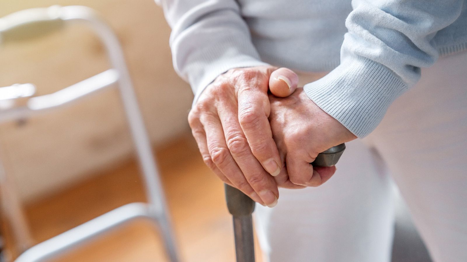 Las manos de una mujer con enfermedad de Parkinson sostienen un bastón para caminar