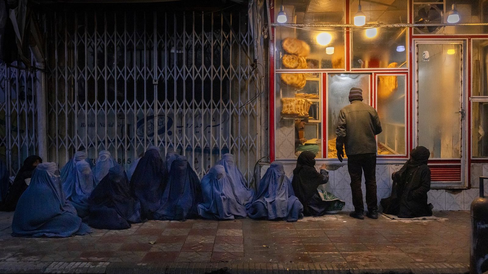 Mujeres y niños piden pan en la puerta de una panadería en Kabul.