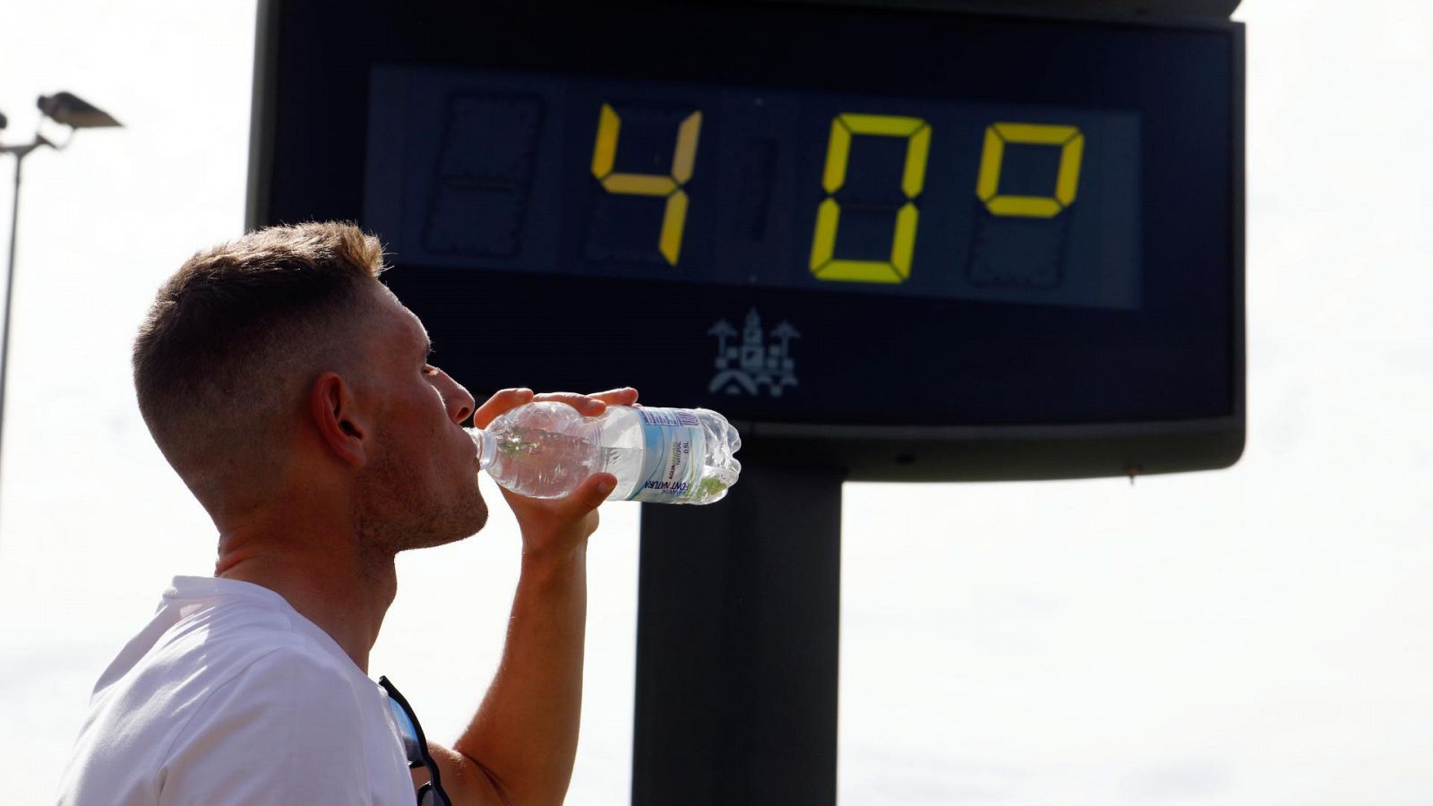 Un joven bebe agua junto a un termómetro en Córdoba que marca 40 grados a finales de abril.