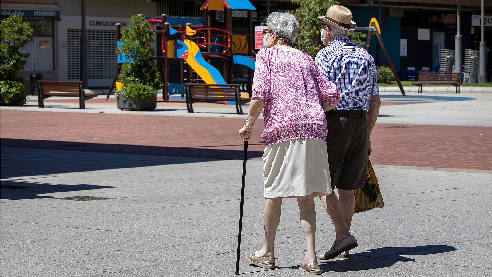 Una pareja de ancianos pasea agarrada del brazo y vestidos con ropa veraniega