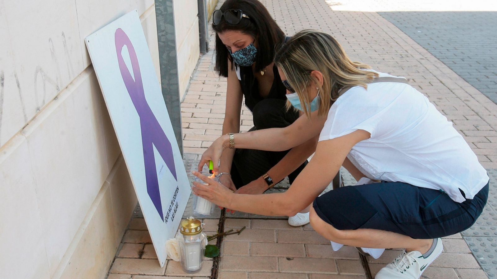 Dos mujeres colocan un cartel con un lazo violeta, símbolo de la violencia machista