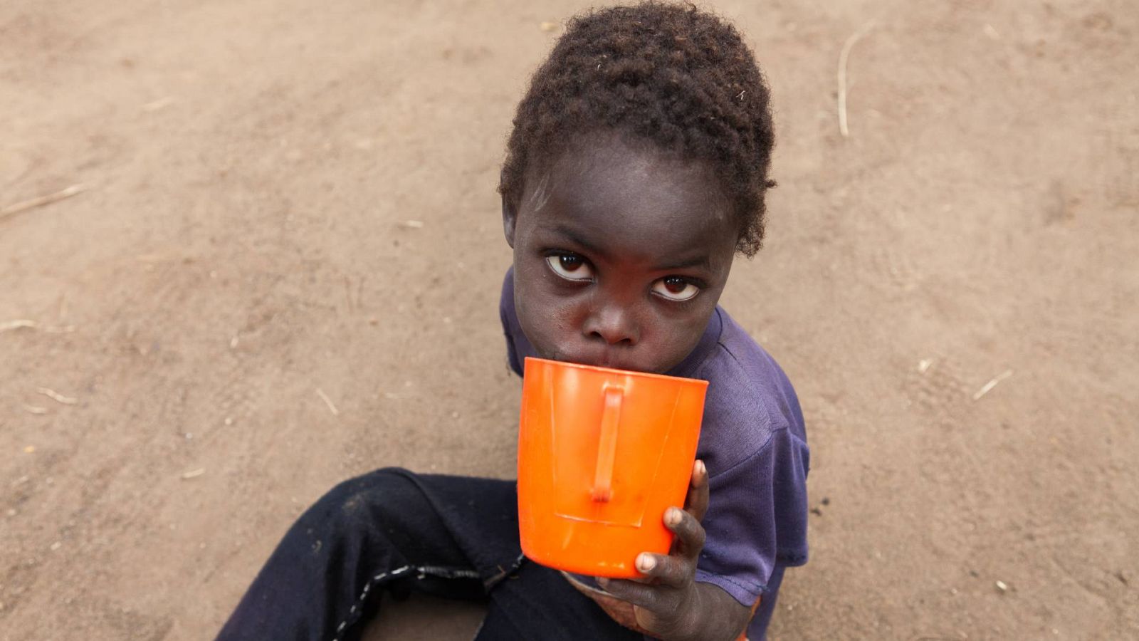 Un niño de bebe agua  en un pequeño pueblo en el distrito sur de Zomba, en Malawi