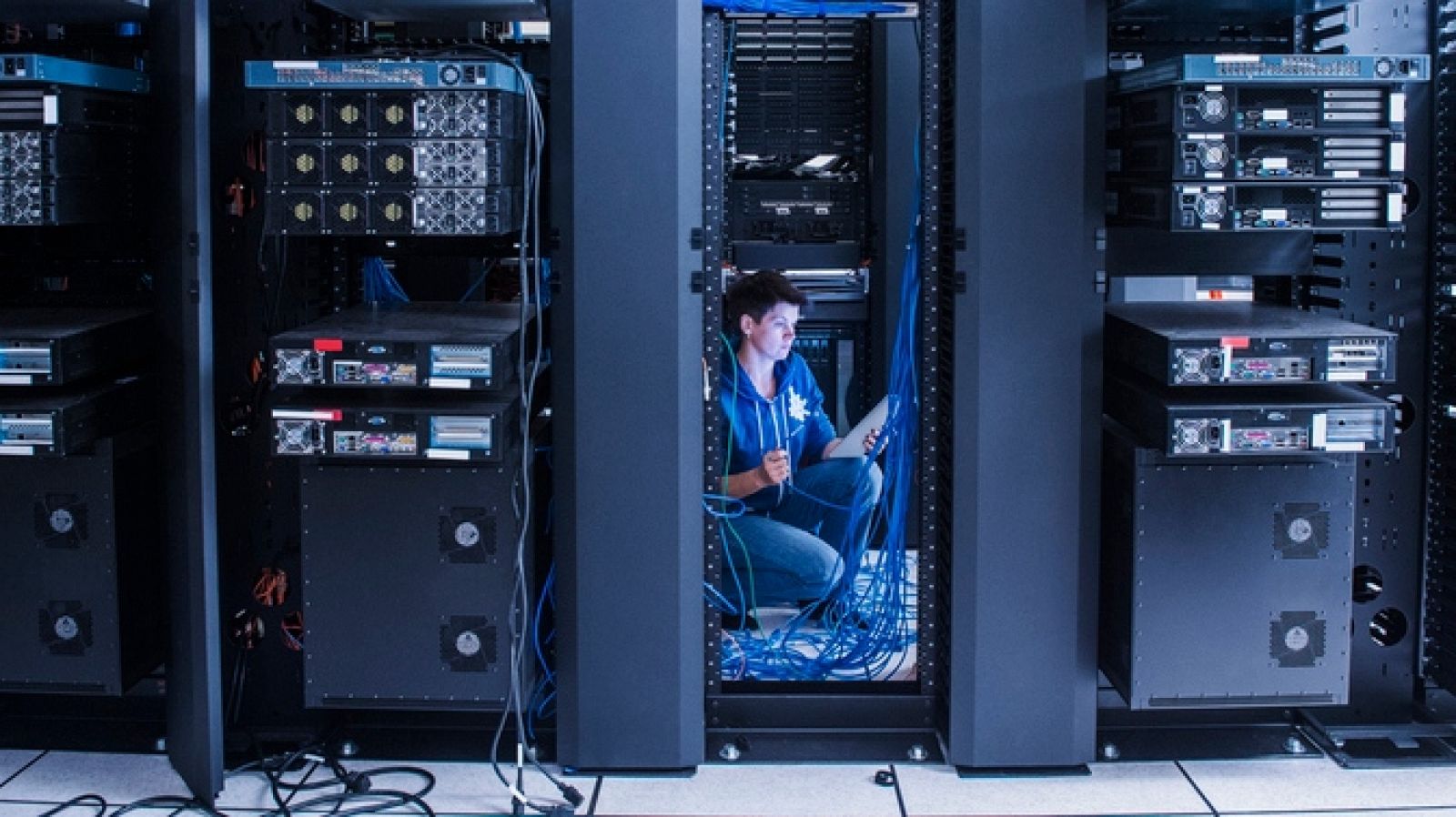Una mujer organizando cables en una zona de servidores y almacenaje de datos.