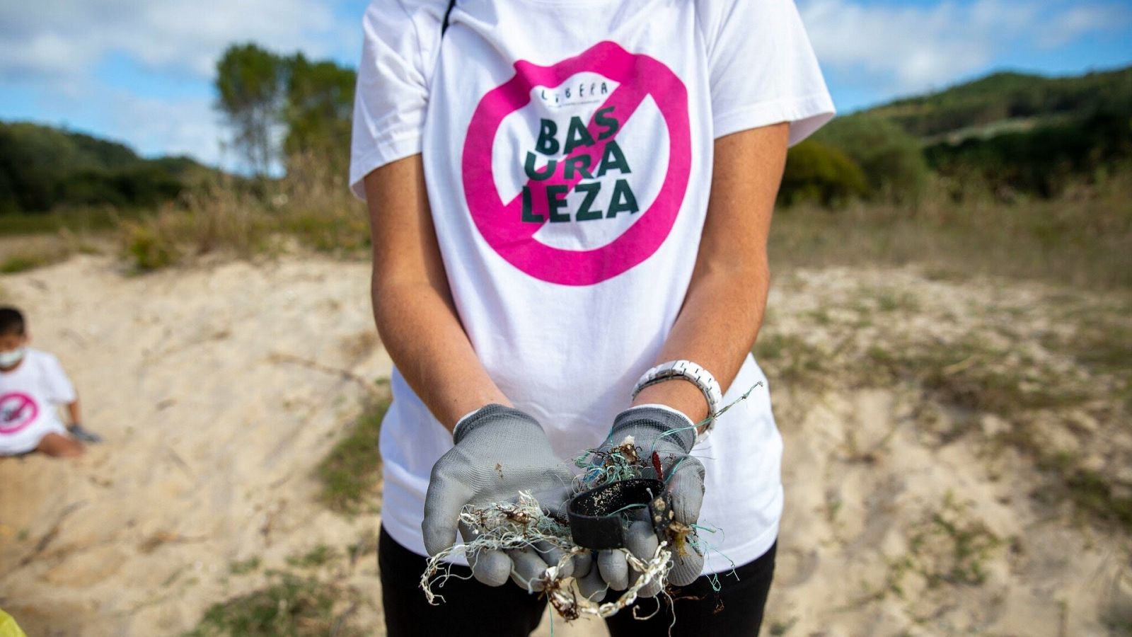 Una mujer con una camiseta de "1 m² contra la basuraleza" recoge residuos en una playa.
