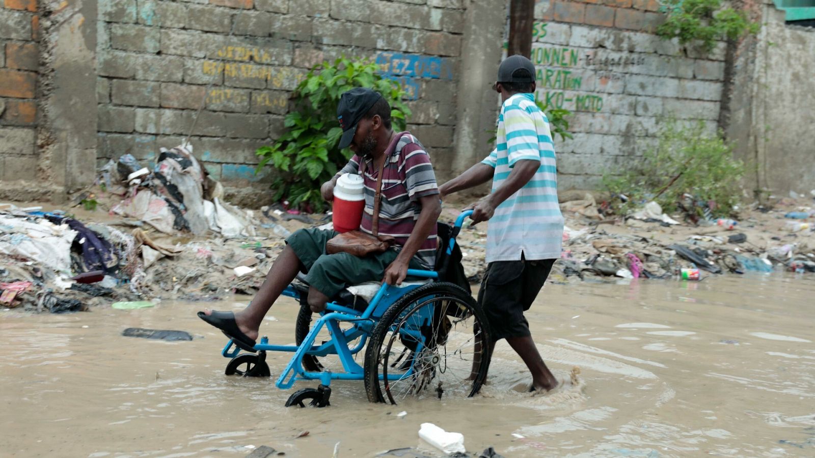 Un hombre ayuda a otro en silla de ruedas a atravesar una calle inundada tras una fuerte lluvia en Puerto Príncipe, en Haití