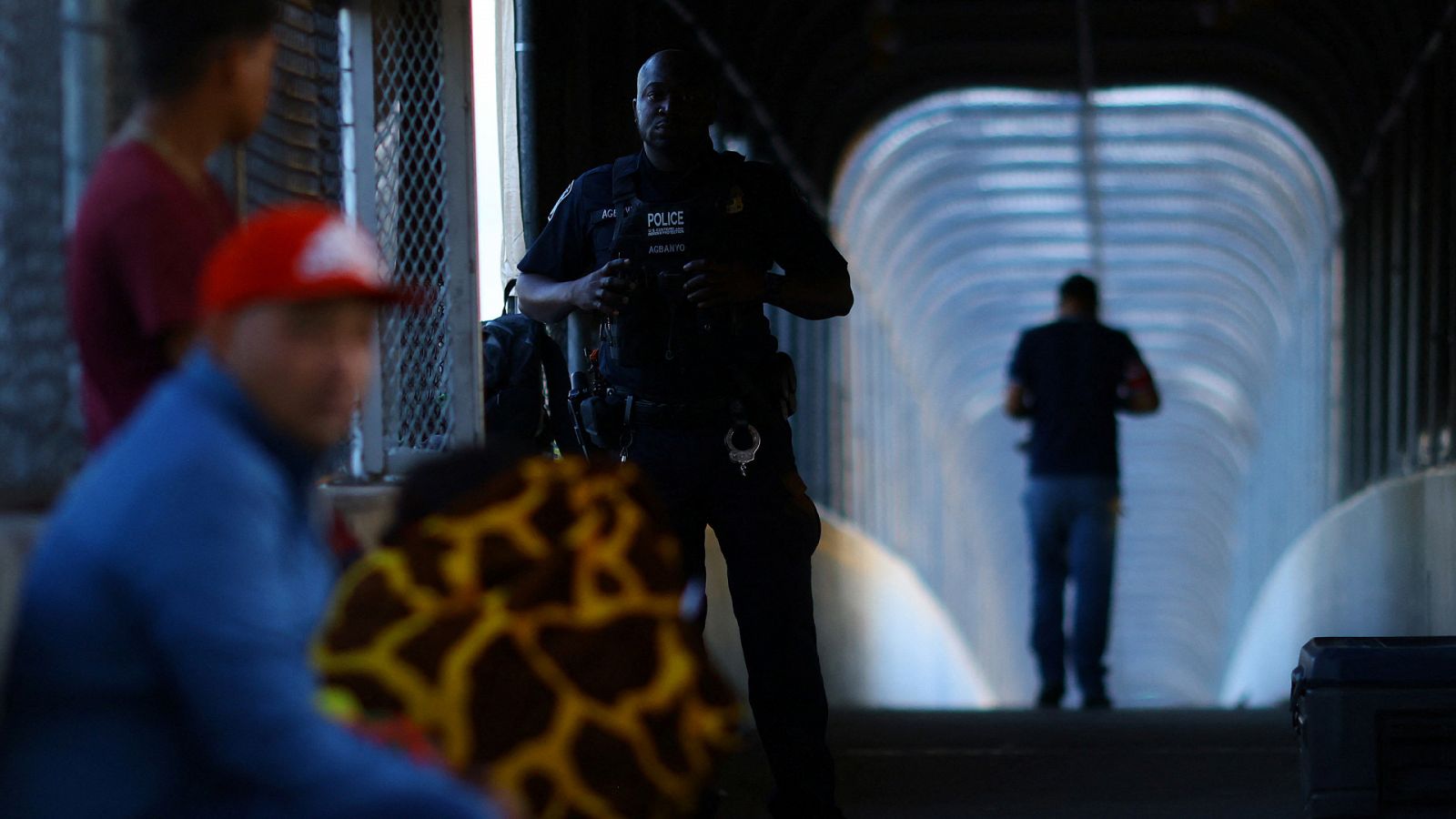 Un agente estadounidense hace guardia mientras migrantes que buscan asilo esperan en el puente internacional de Córdova de las Américas