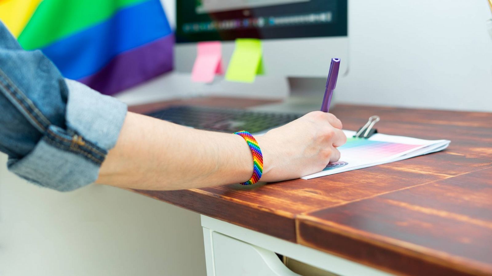 Una persona con una pulsera con la bandera LGTBI+ escribiendo