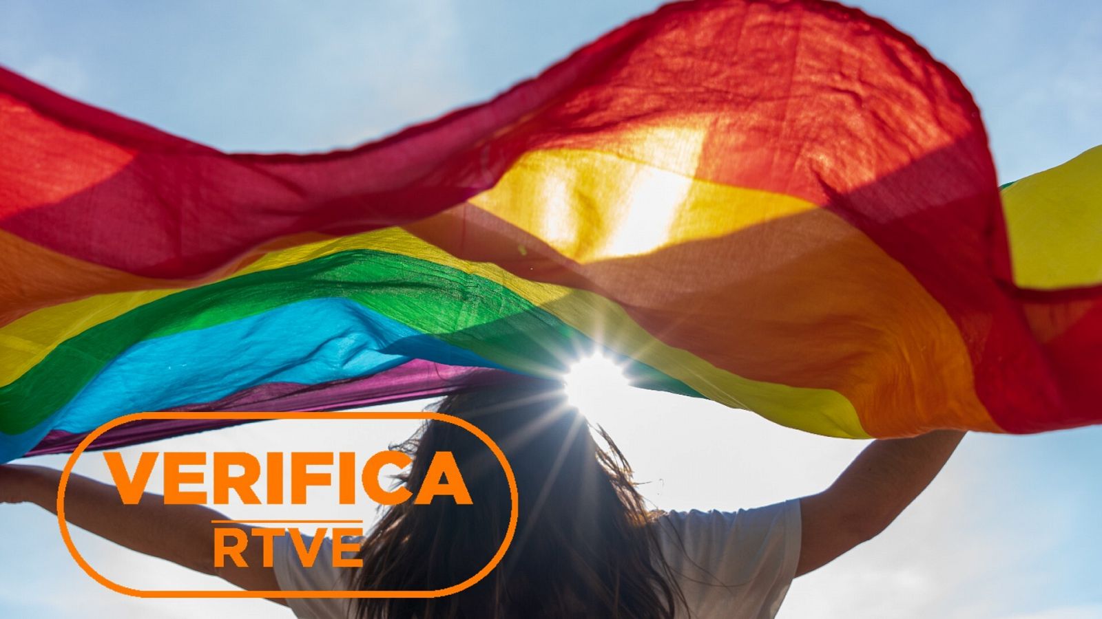 Imagen de recurso de una persona alzando una bandera LGTBI, con el sello VerificaRTVE en naranja