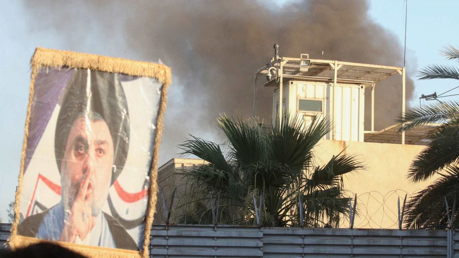 Un manifestante sostiene un retrato del clérigo chií Moqtada al-Sadr mientras sale humo del edificio de la embajada sueca en Irak durante una protesta.