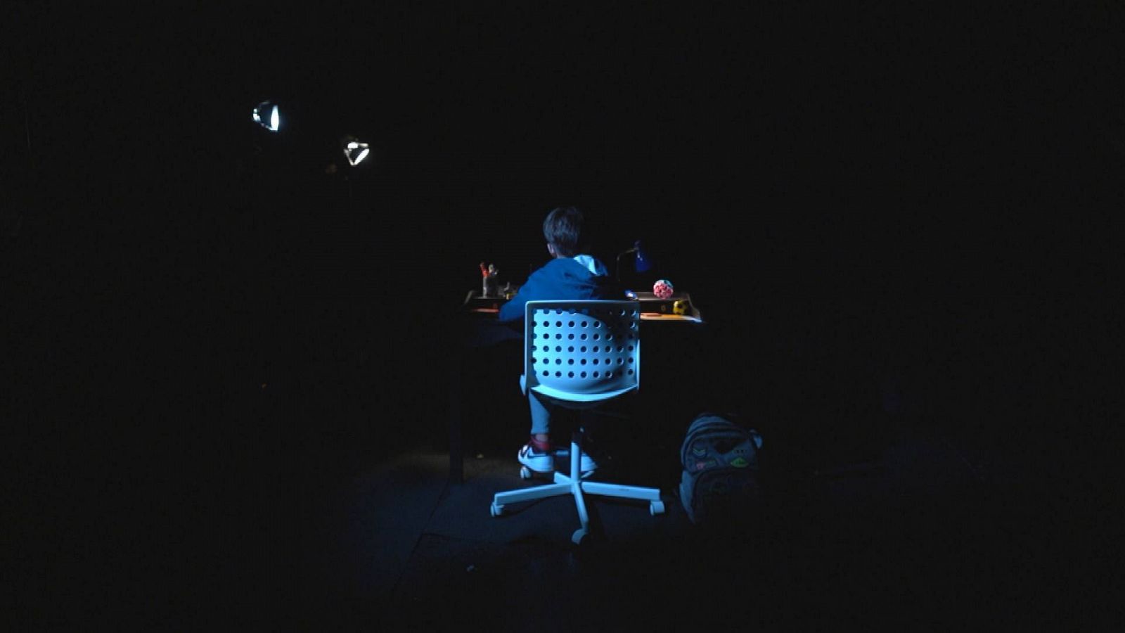 Un niño está sentado frente a la pantalla de un ordenador en una habitación oscura.
