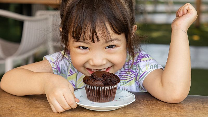 Una niña come una magdalena de chocolate Una niña come una magdalena de chocolate
