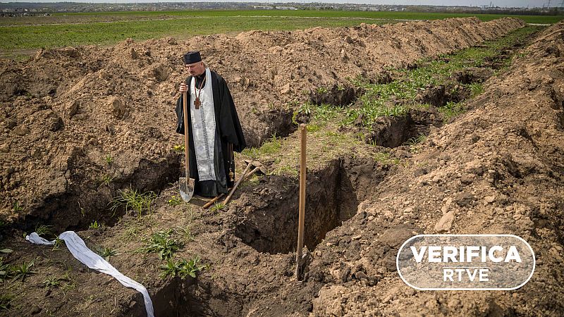 Imagen de la agencia EFE donde un religioso observa una de las fosas durante el entierro de un soldado ucraniano, con el sello VerifcaRTVE en blanco