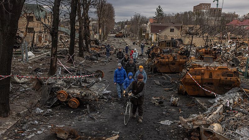 Residentes pasan junto a maquinaria militar rusa destruida en una calle de Bucha
