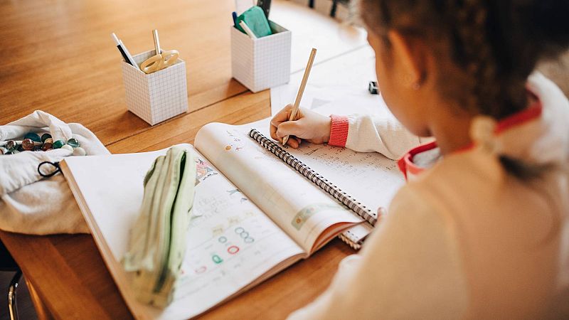 El debate de los deberes en verano: Una niña haciendo tareas escolares en un imagen de archivo El debate de los deberes en verano: Una niña haciendo tareas escolares en un imagen de archivo